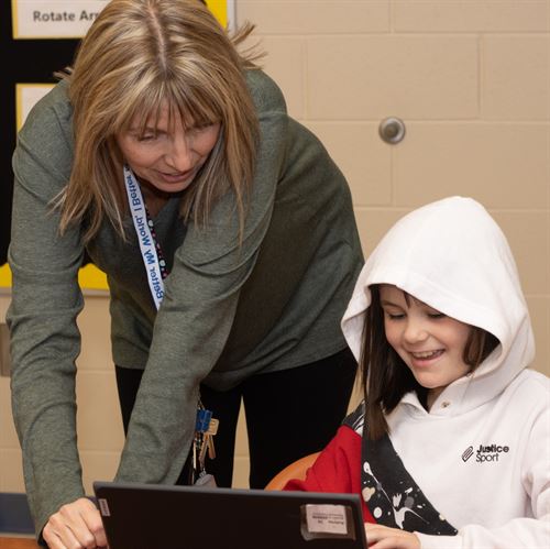 teacher in gray shirt helping student in white sweat shirt on laptop